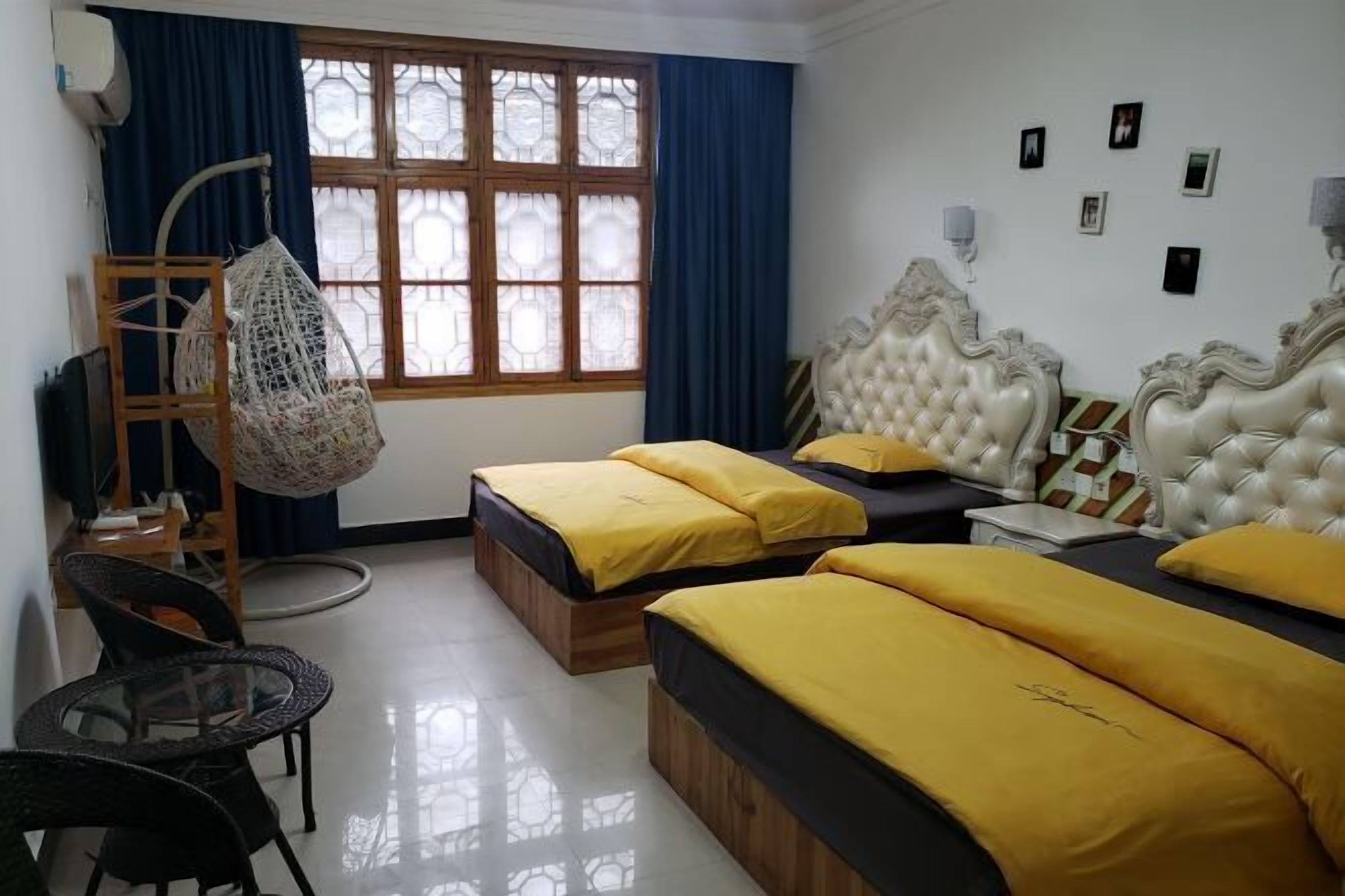 A hotel room with two beds, a hanging chair, a small table, and a window with curtains.
