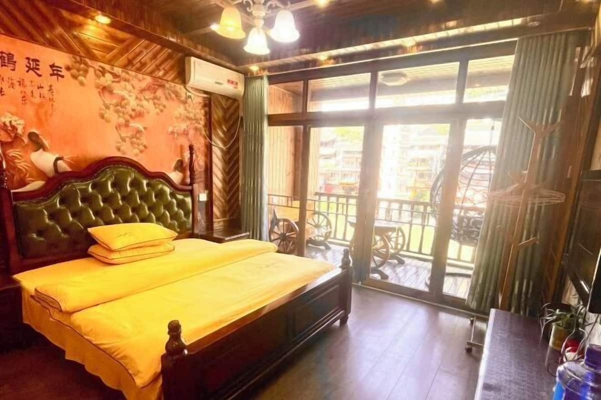 A room with a bed, a window with a view, a wall with a decorative pattern, and a ceiling fan.