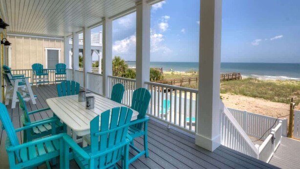 Un espace extérieur abrité, doté d’une table et de chaises, offrant une vue sur la plage et comprenant une terrasse en bois.