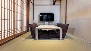 A traditional Japanese room with tatami flooring, a low table with cushions, and a TV mounted on the wall. - Kai  (Kyoto)