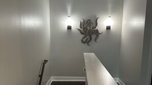 A staircase with dark wooden steps and white trim, leading to a landing with a light-colored wall and a decorative wall piece. - Charming 2bed, 2bath condo on The Strand, Galveston with WiFi, AC, garage (Galveston)
