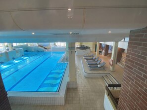An indoor swimming pool with clear lanes, a sun deck with lounge chairs, and a view of the pool area.