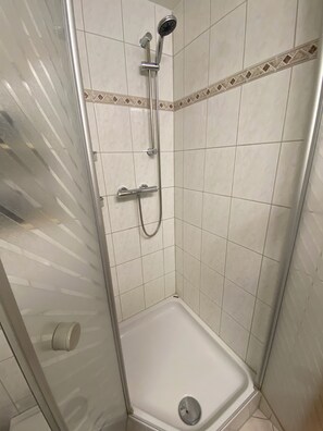 Eine Dusche mit Handbrause und Handtucharmatur, ein Eck-Duschbereich mit Abfluss und geflieste Wände mit dekorativer Bordüre.