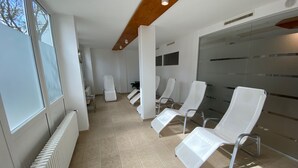Een wachtruimte met witte stoelen, een radiator en een glazen wand.