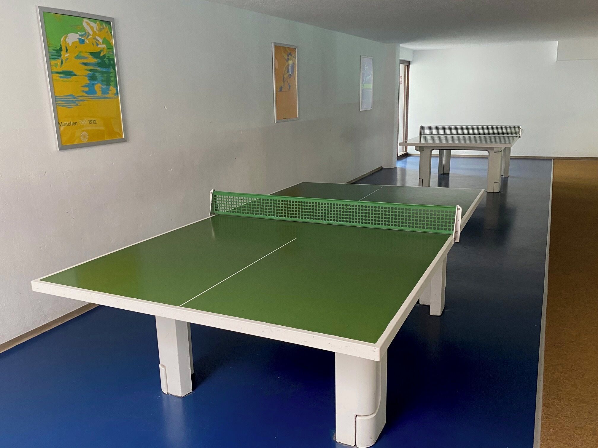 Ein Zimmer mit einem Pingpongtisch, einer Bank und zwei gerahmten Bildern an der Wand.