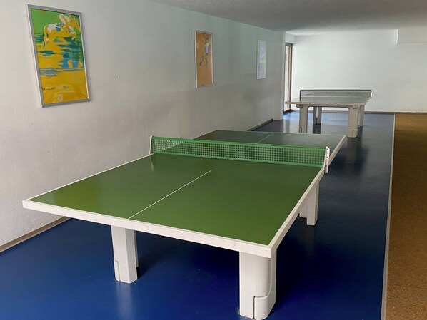 A room with a ping pong table, a bench, and two framed pictures on the wall.