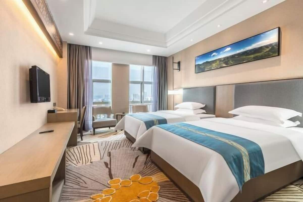 Une chambre d’hôtel avec deux lits, un bureau, une télévision et une grande fenêtre donnant sur la ville.