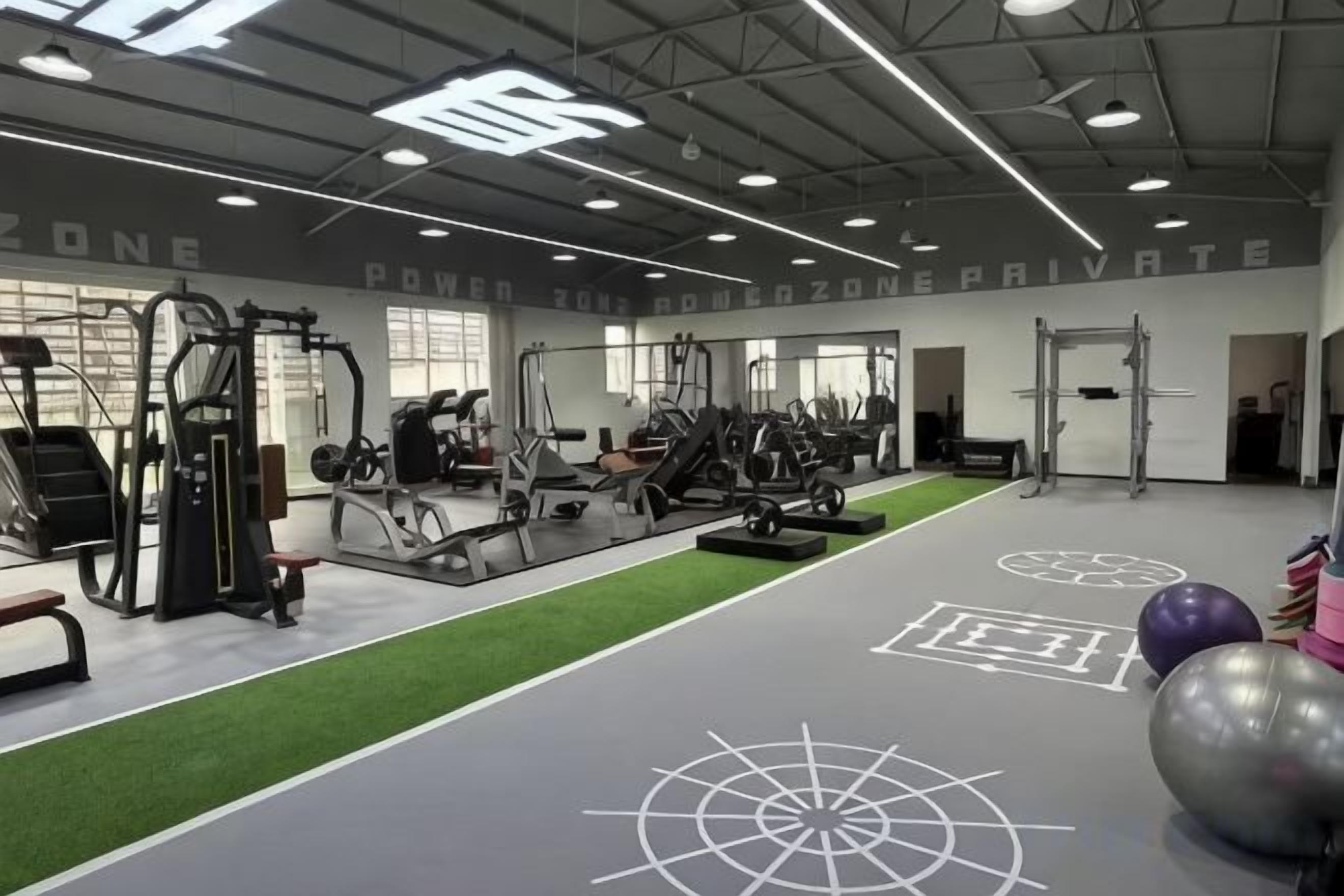 Une salle de sport équipée de divers appareils d’exercice, dotée d’une zone de tapis synthétique vert et d’un mur sur lequel est inscrit le texte « ZONE DE FORCE ».