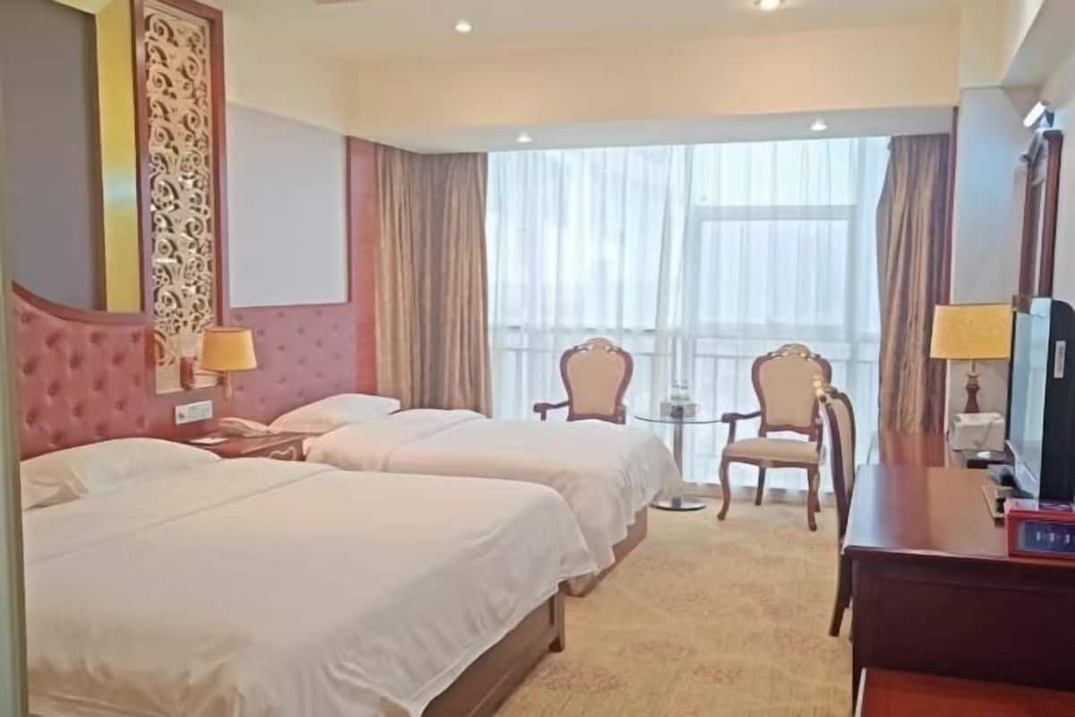 Une chambre d’hôtel avec deux lits, un bureau, une chaise, une petite table et un téléviseur.