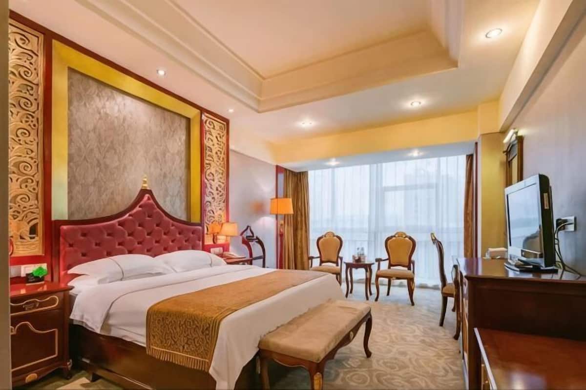Une chambre d’hôtel avec un grand lit, un bureau avec un ordinateur, une télévision et une vue sur la ville.