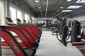 Un gimnasio con cintas de correr, máquinas de pesas y un espejo grande.