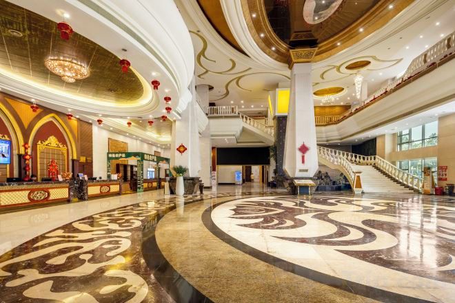 A spacious lobby with a grand staircase, a reception area, and a decorative floor pattern.