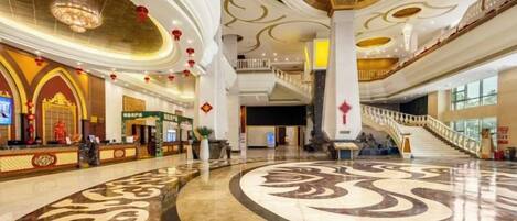 A spacious lobby with a grand staircase, a reception area, and a decorative floor pattern.
