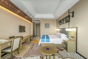 Una habitación de hotel con cama, mesita de noche, escritorio, silla y una pequeña mesa redonda.