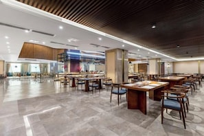 A spacious dining area with multiple tables and chairs, a modern ceiling design, and a large window providing natural light. - Chuanyu Huisen Hotel (Baise)