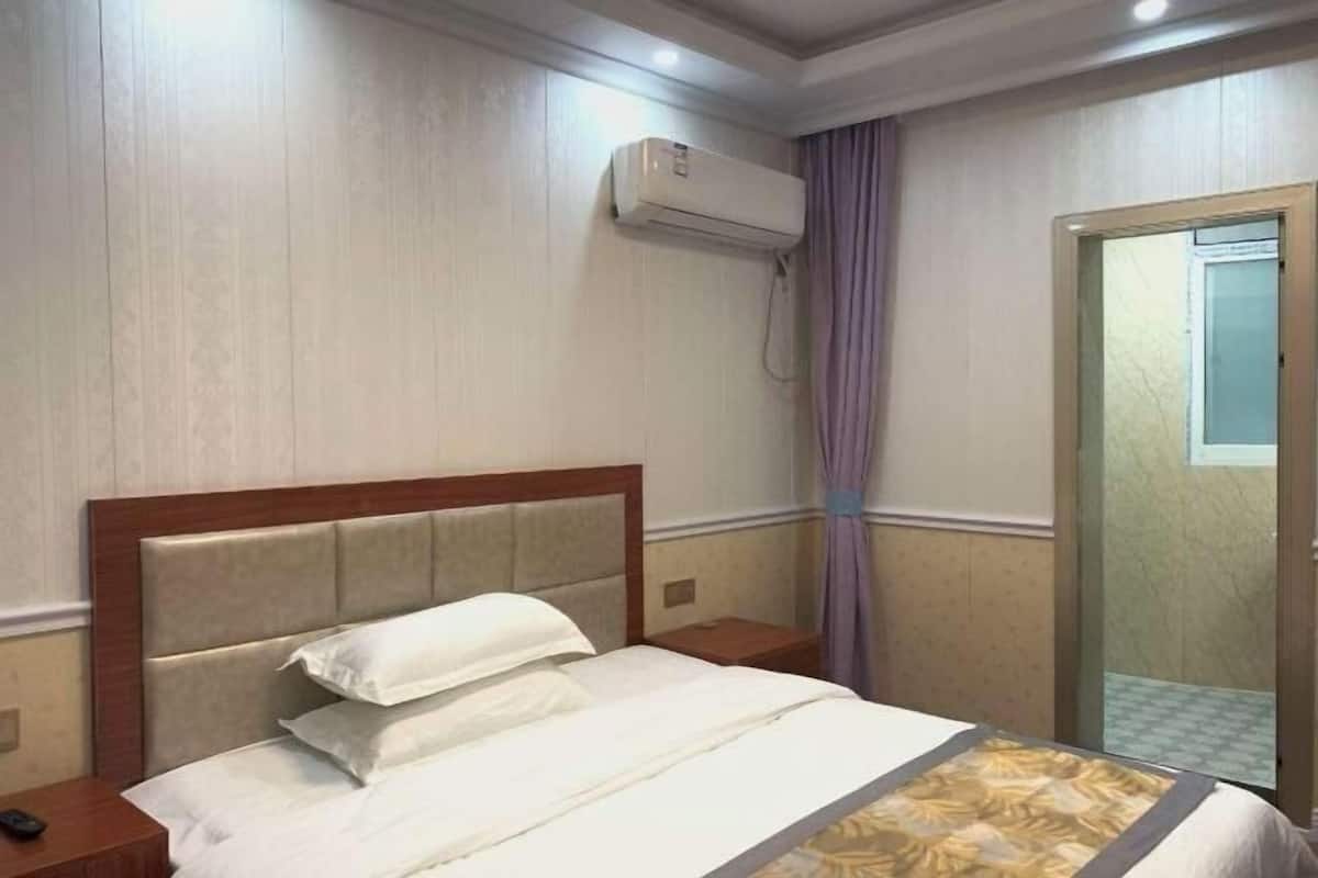 A hotel room with a bed, a nightstand, an air conditioning unit, and a door with a glass panel.