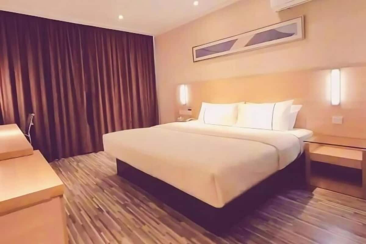 A hotel room with a large bed, wooden flooring, a headboard with wall-mounted lights, and a dark curtain.