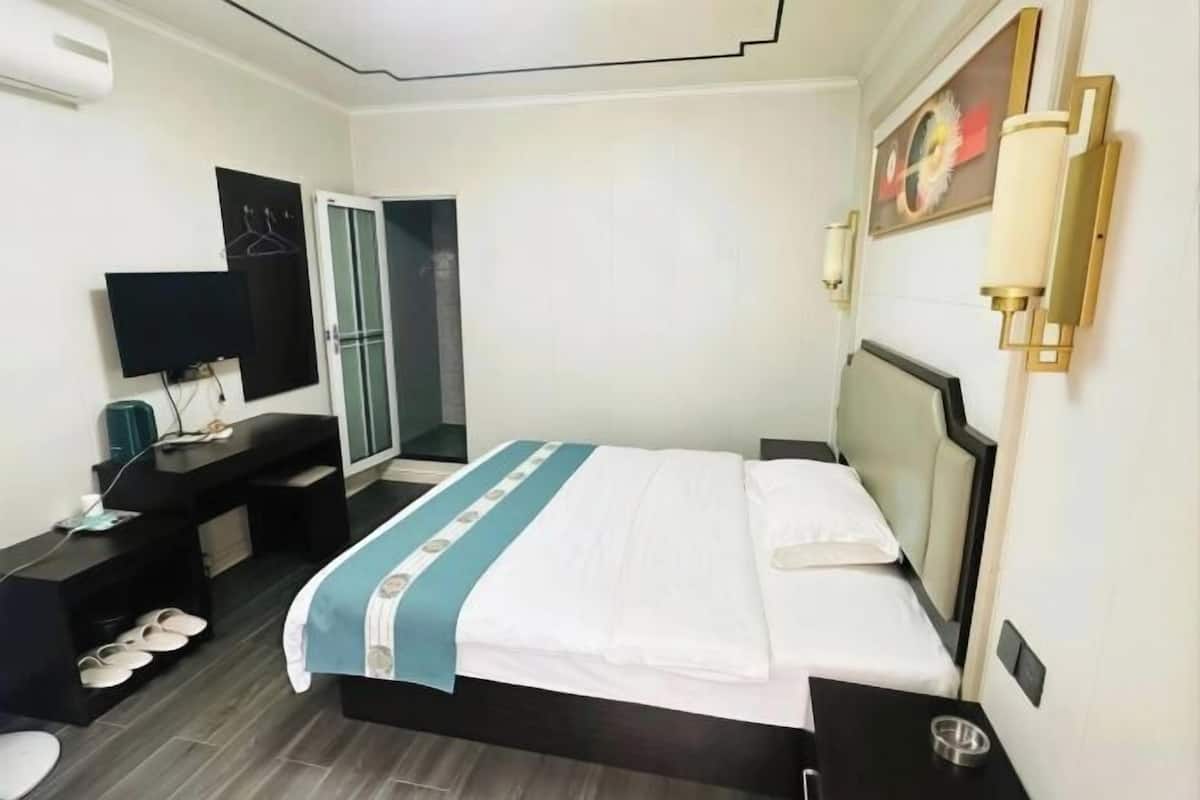 A hotel room with a bed, a desk with a flat-screen TV, a mirror, and a wardrobe.