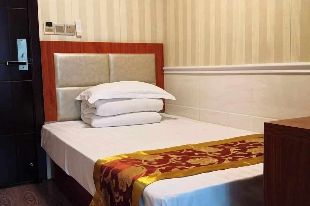 A hotel room with a bed, a wooden headboard, a bedside table, and a wall-mounted control panel.