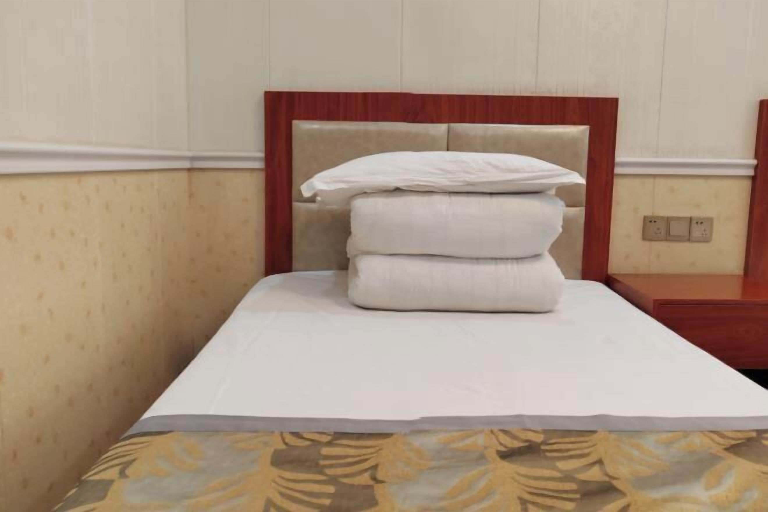 A neatly made bed with a wooden headboard, a white pillow, and a folded blanket.