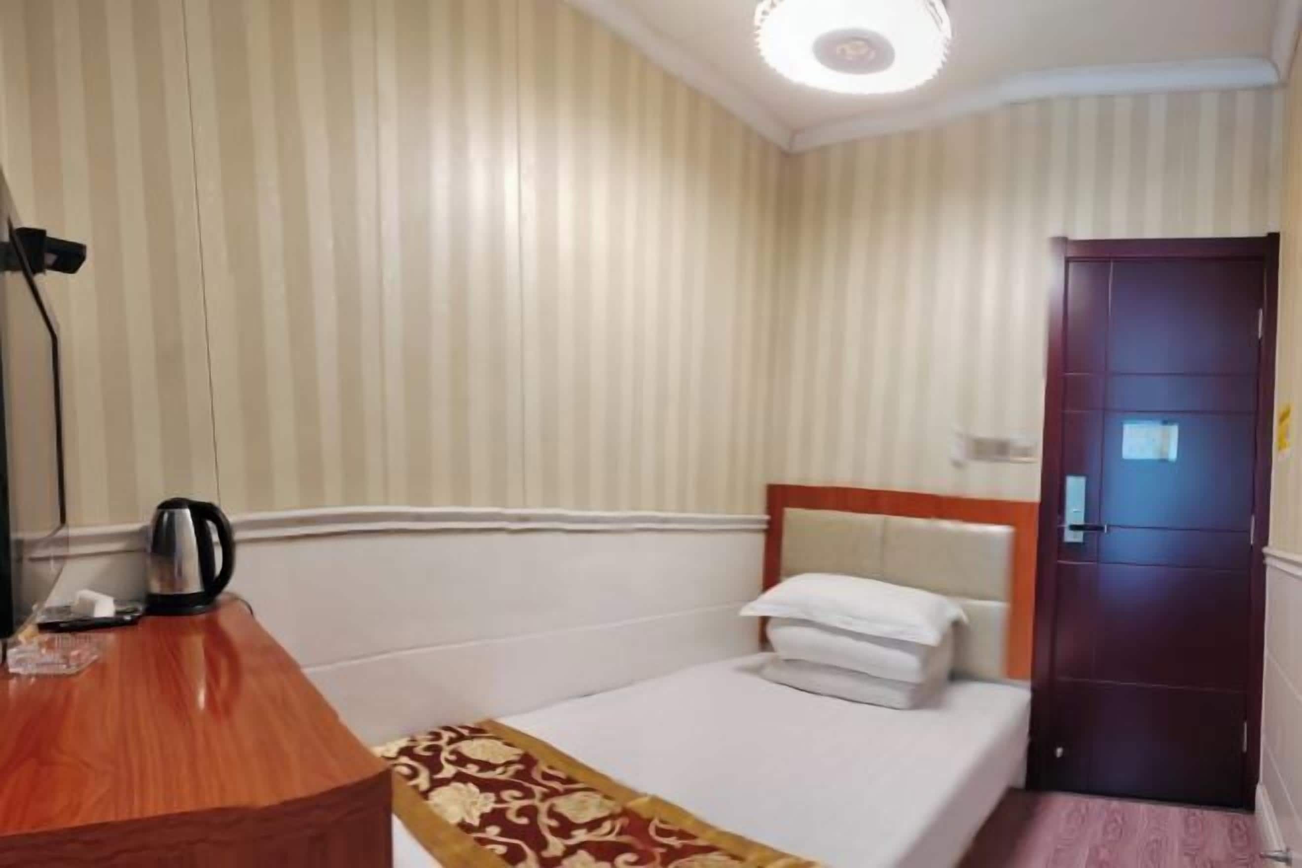 A hotel room with a single bed, a wooden desk, a kettle, and a door.