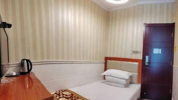 A hotel room with a single bed, a wooden desk, a kettle, and a door.