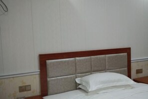 A hotel room with a wooden headboard, a white bedspread, and a nightstand with a lamp. - Fuan Hotel (Jiujiang)