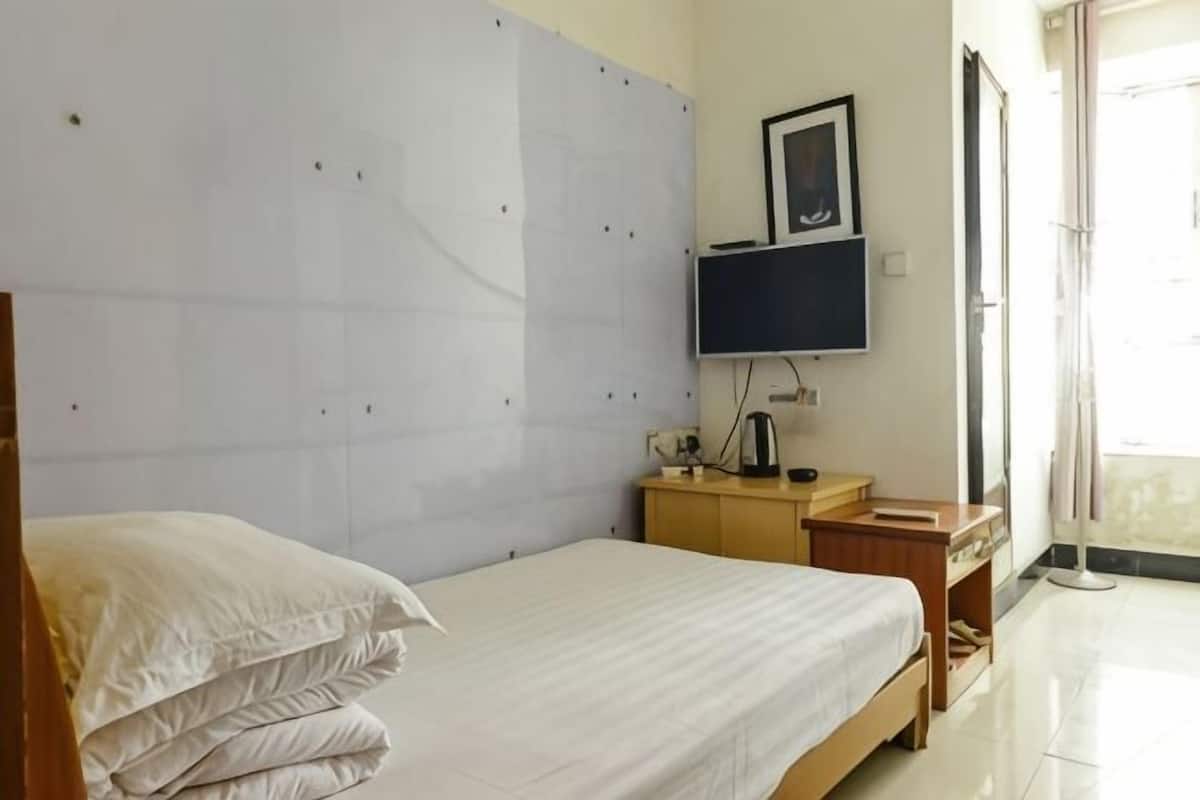 A bedroom with a bed, a television, a wooden nightstand, and a window.