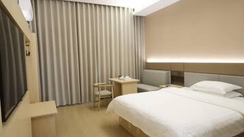 A hotel room with a bed, bedside table, chair, and a TV.