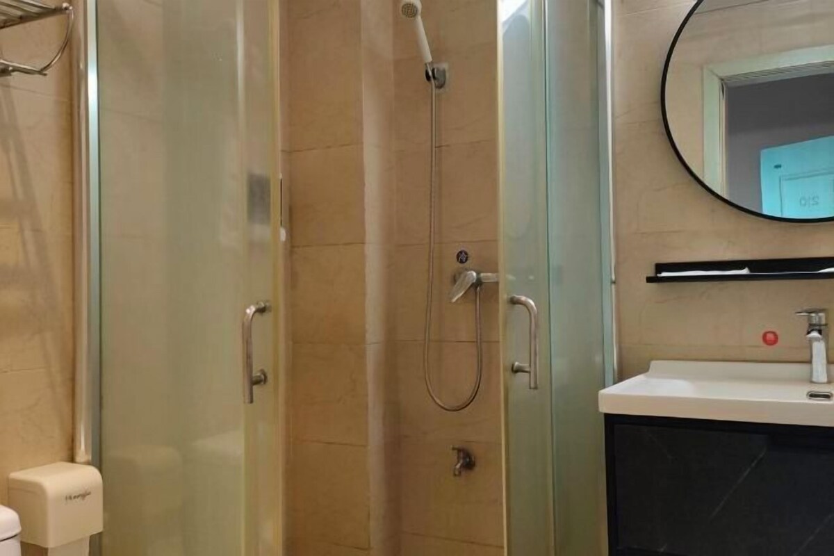 A modern bathroom with a glass-enclosed shower, a sink with a mirror, and a soap dispenser.