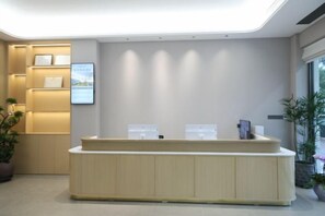 A reception desk with a modern design, a wall-mounted television, and a potted plant to the left. - Dongshan Huatian Business Hotel (Dongshan County)