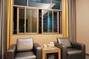 Una habitación con dos sillones de cuero, una mesita con un cuenco y una tetera, y una ventana con cortinas.