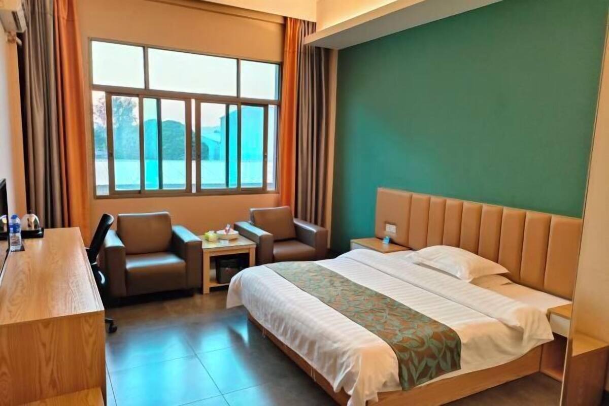 A hotel room with a bed, two chairs, a desk, and a window with curtains.