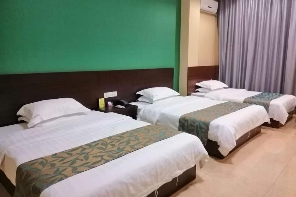 A hotel room with three beds, a green wall, a wooden headboard, and a grey curtain.