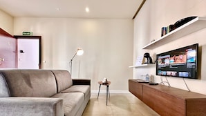 Una sala de estar moderna con un sofá, una mesa de centro, un televisor montado en la pared y una estantería.