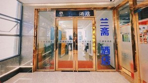 A hotel entrance with a glass door, a sign above the door, and a reflection of the interior. - Penglai Hotel (Shenzhen)
