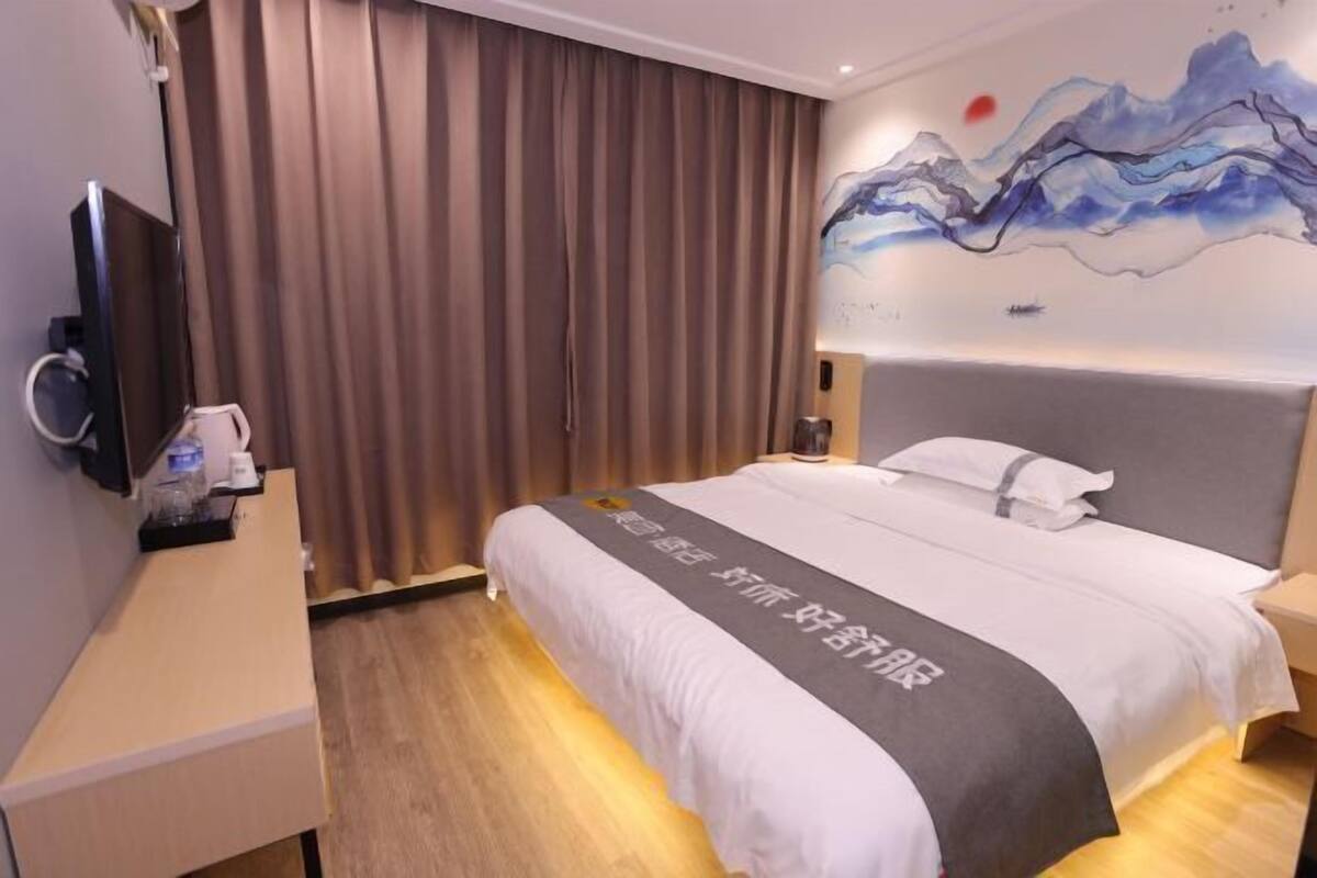 A hotel room with a bed, a TV, a desk with a phone, and a painting on the wall.