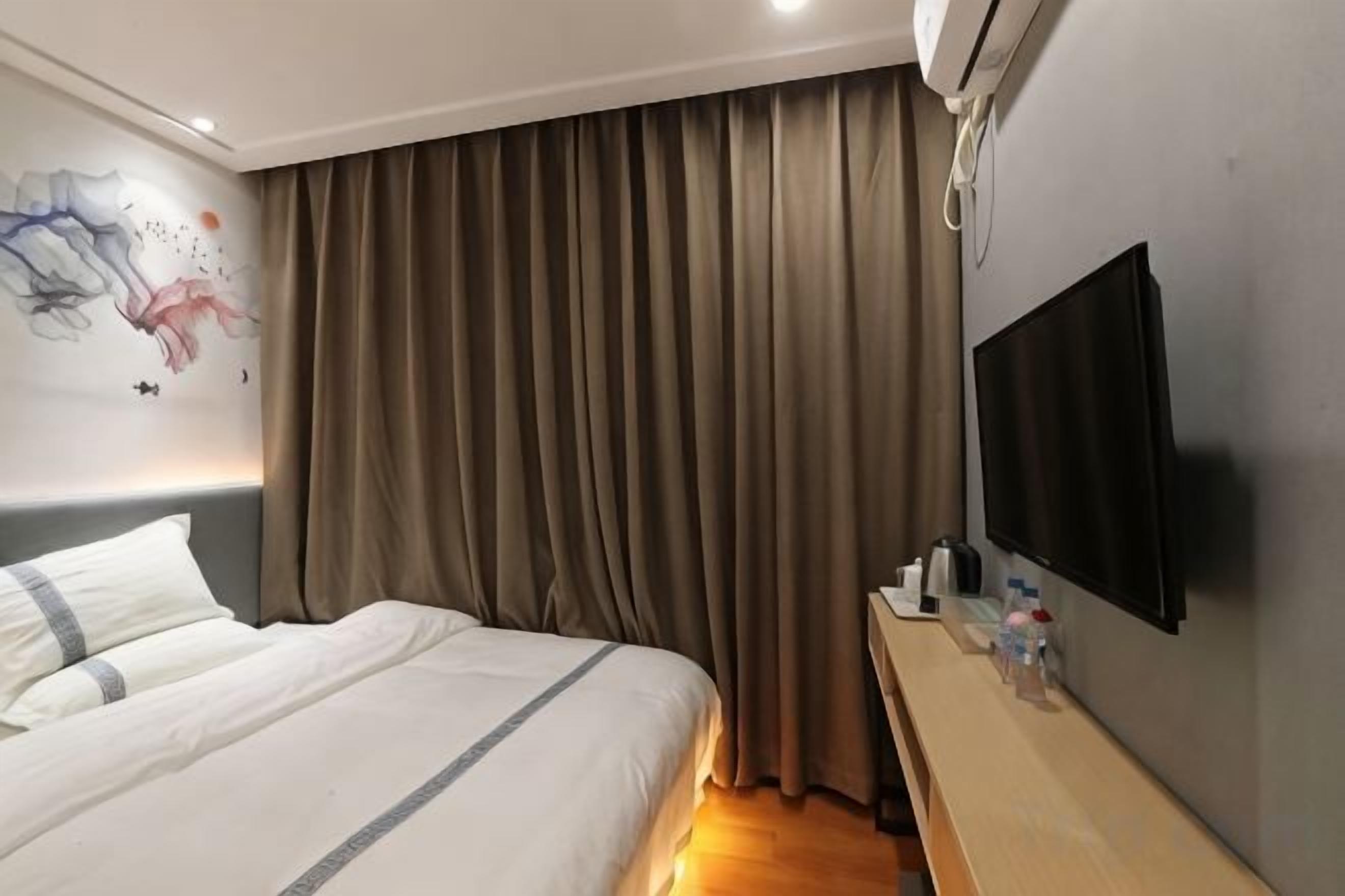 A hotel room with a bed, a flat-screen TV, a bedside table, and a wall-mounted air conditioning unit.