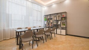 A modern meeting room with a long table and chairs, a bookshelf, and a large window with sheer curtains. - Penglai Hotel (Shenzhen)