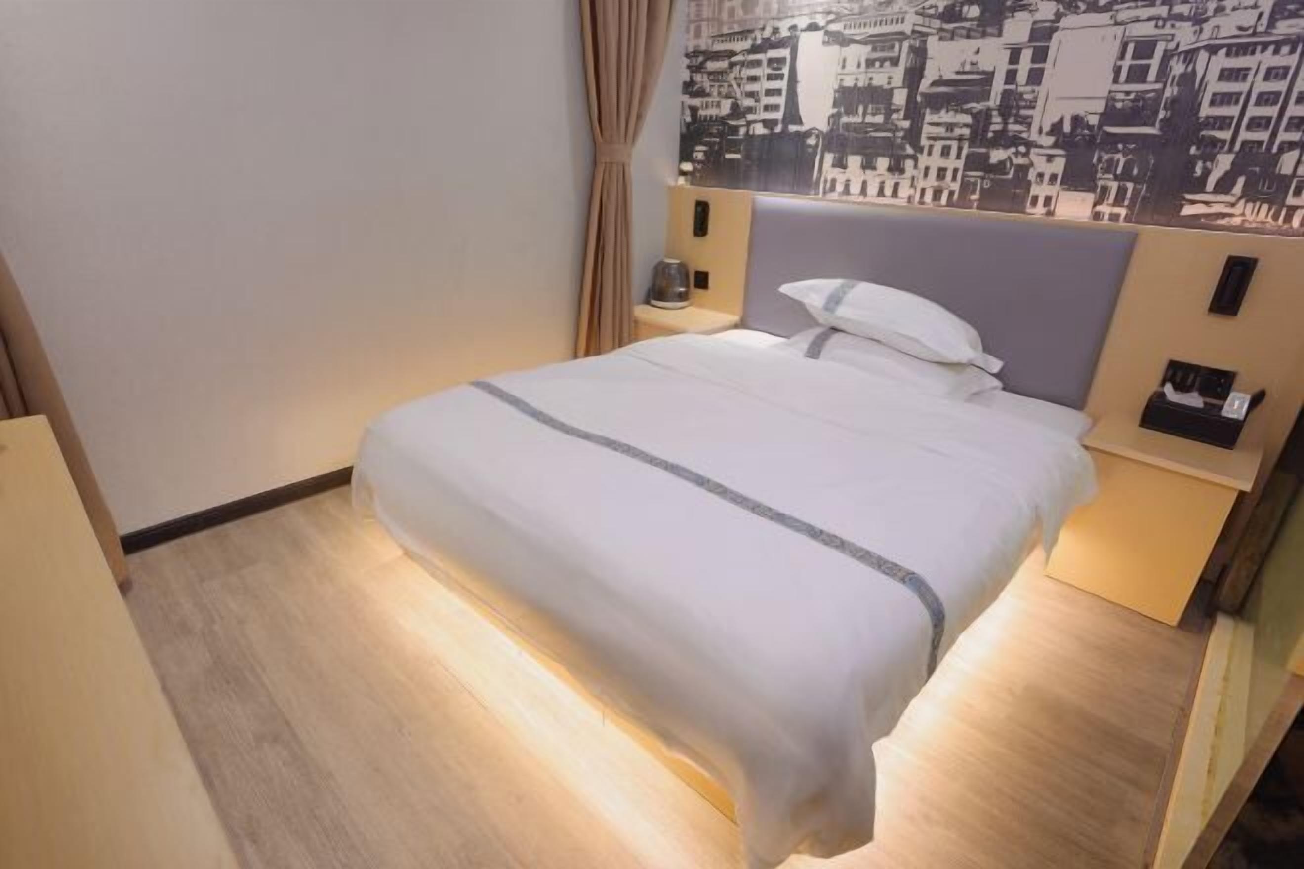 A hotel room with a bed, nightstands, a wall-mounted telephone, and a cityscape mural.