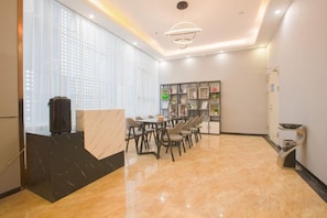 A modern hotel lobby with a marble floor, a reception desk, and a dining area with chairs and tables.