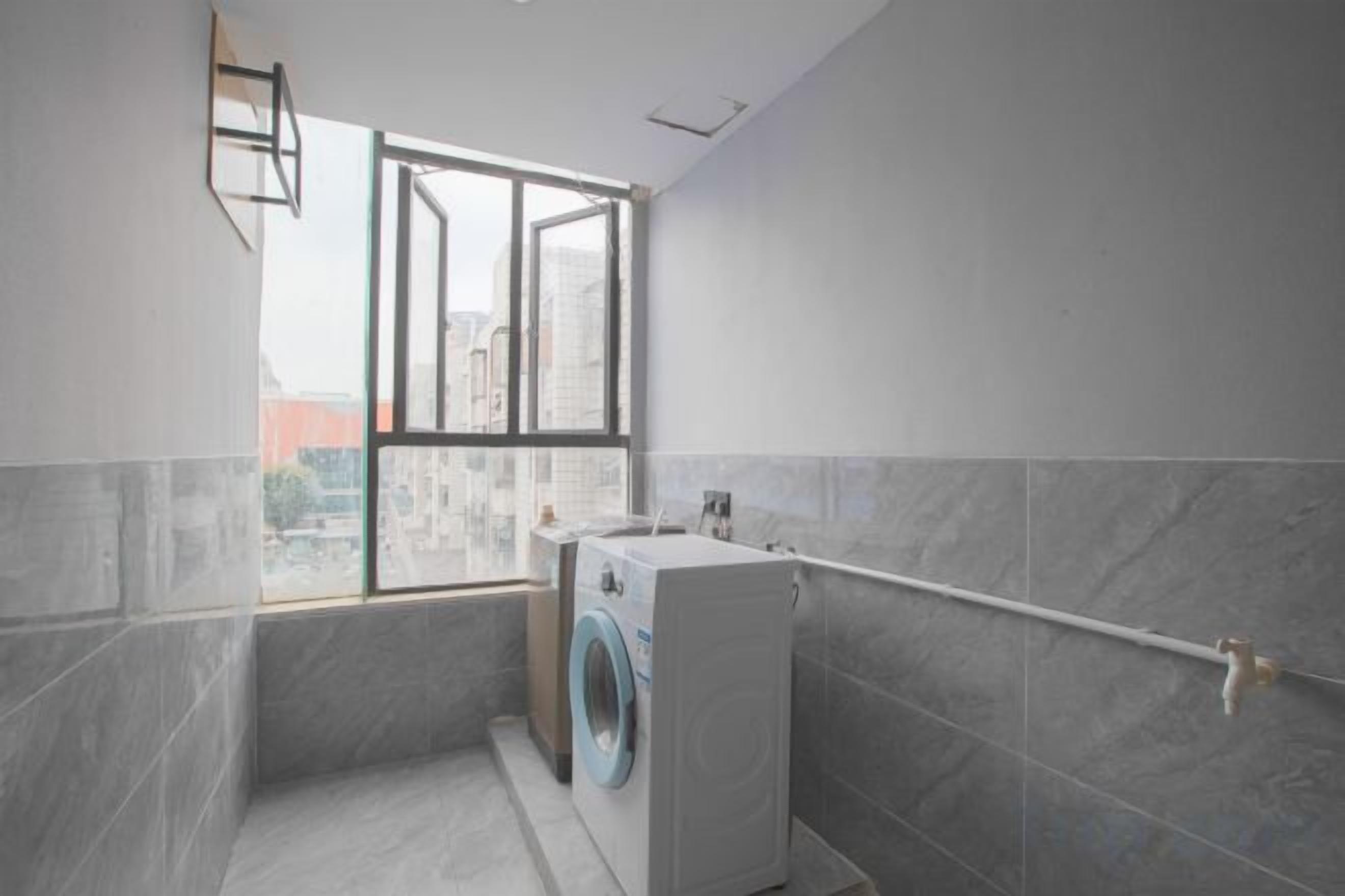 A laundry room with a washing machine, a drying rack, and a window with a view of buildings.