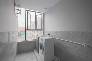 A laundry room with a washing machine, a drying rack, and a window with a view of buildings. - Penglai Hotel (Shenzhen)