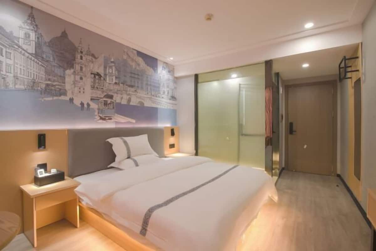 A hotel room with a bed, bedside table, wall art, and a glass door leading to a bathroom.