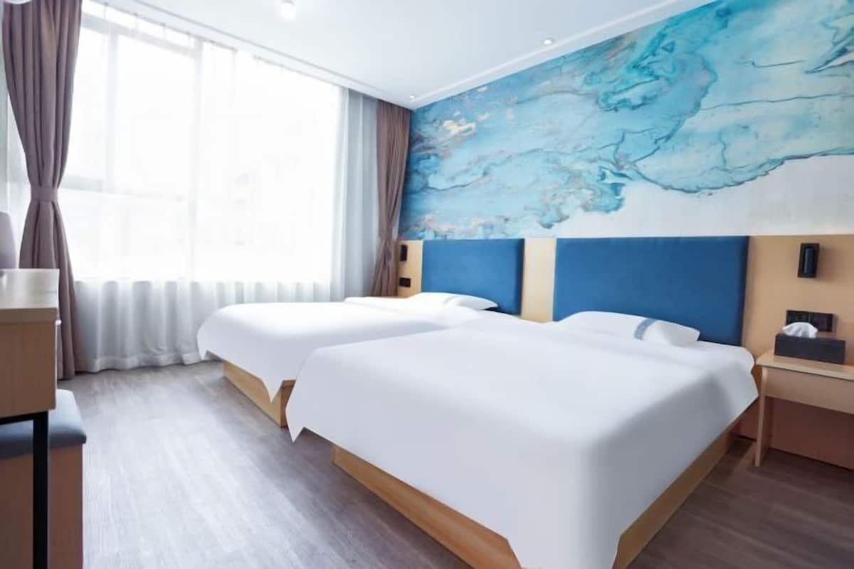 A hotel room with two beds, a large abstract painting on the wall, and a view of the city through the window.