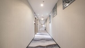 A long, narrow hallway with a patterned carpet, white walls, and a ceiling with recessed lighting. - Penglai Hotel (Shenzhen)