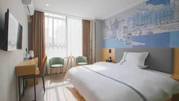 Quarto de hotel com uma cama grande, uma escrivaninha com cadeira, uma mesinha com duas cadeiras e uma janela ampla com cortinas.