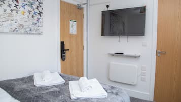 A hotel room with a bed, two rolled towels, a wall-mounted TV, a door with a lock, and a wall with a decorative butterfly pattern.
