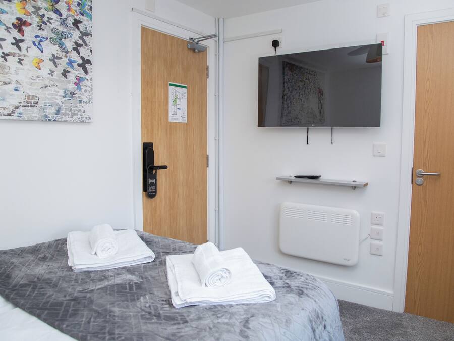 A hotel room with a bed, two rolled towels, a wall-mounted TV, a door with a lock, and a wall with a decorative butterfly pattern.