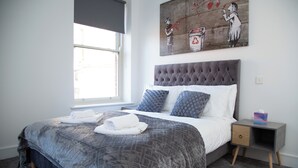 Ein Schlafzimmer mit einem Bett, einem Fenster, einem Nachttisch und einem Bild an der Wand.